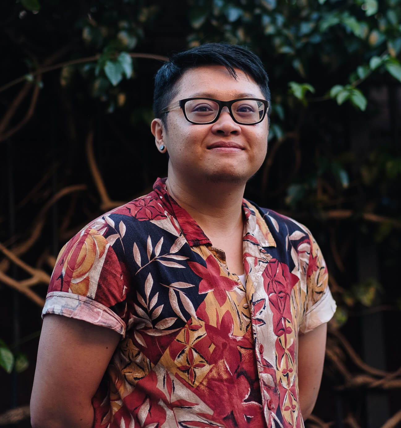 Headshot of artist Kiki of Introspective Arts standing arms crossed in front of some leafy scenery.
